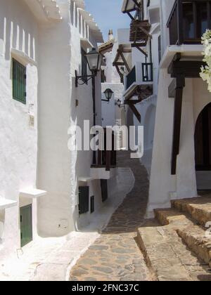 Typical Spanish construction of a narrow alley between white beach houses built according to Cycladic architecture in Menorca. Stock Photo