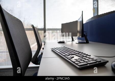 Chairs and dual monitors in an office, empty while people work from home during the covid pandemic. Bright open large window letting sunlight through. Stock Photo