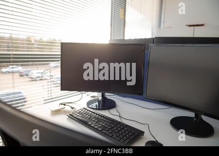 Chairs and dual monitors in an office, empty while people work from home during the covid pandemic. Bright open large window letting sunlight through. Stock Photo