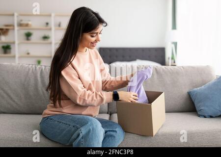 Smiling young woman unpacking parcel after online shopping Stock Photo