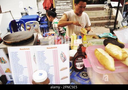 Lao man in local grocery shop sale french loaf or baguette sandwich for laotian people and foreign travelers travel visit at Louangphabang Street Nigh Stock Photo