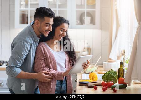 Happy Arab Spouses With Digital Tablet In Kitchen Searching Meal Recipe Online Stock Photo