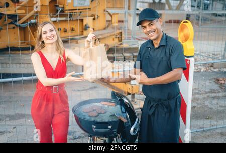Cook handing woman customer a burger in bag for takeout Stock Photo