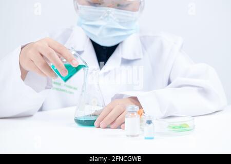 A little scientist is pouring blue liquid chemical in Erlenmeyer flask isolated on white background. Science experiment and education concept Stock Photo