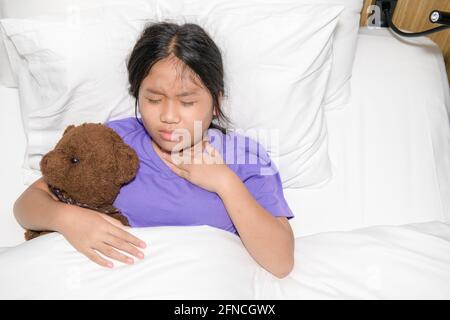 Little girl with sore throat holding toy bear abd lying on bed, health care concept Stock Photo