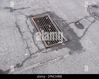 Rusty storm drain grate in cracked asphalt Stock Photo