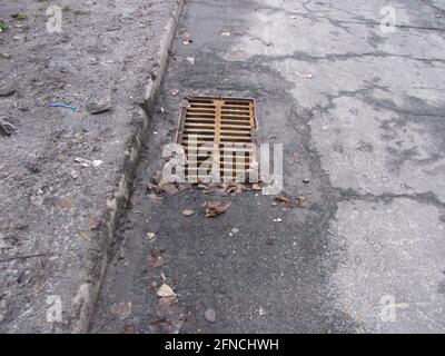 Rusty storm drain grate in cracked asphalt Stock Photo