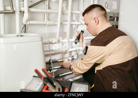 A man in uniform using handtool while repairing pipe in lavatory Stock Photo