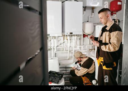 Young repairman using digital tablet against his colleague repairing pipes Stock Photo