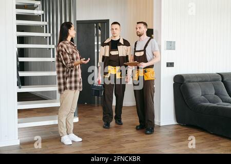 Two plumbers and young female having conversation about plumbing problems in living-room Stock Photo