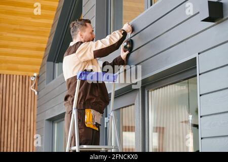 Young man in uniform holding alarm system while standing on ladder Stock Photo