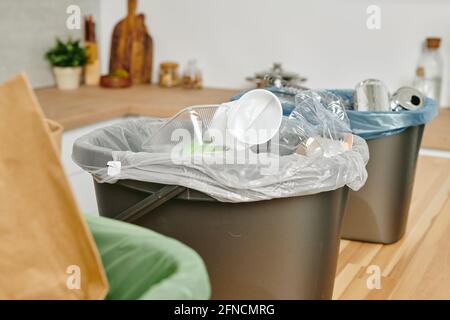A plastic bag with used disposable kitchenware and other waste in trash bin on wooden table Stock Photo