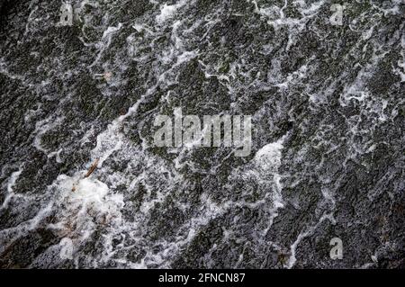 water flowing over black stones of a weir Stock Photo