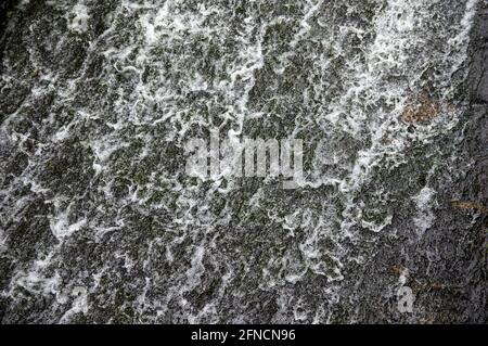water flowing over black stones of a weir Stock Photo