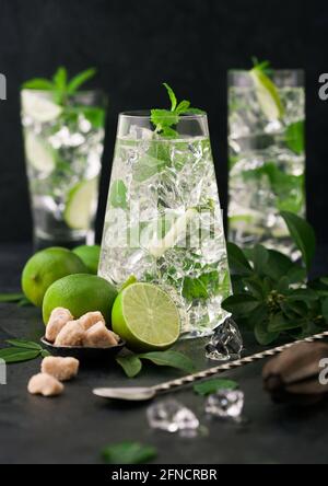 Glasses of Mojito cocktail with ice cubes,mint and lime on black board with spoon and fresh limes with cane sugar. Best party drink.Sparkling mint wat Stock Photo