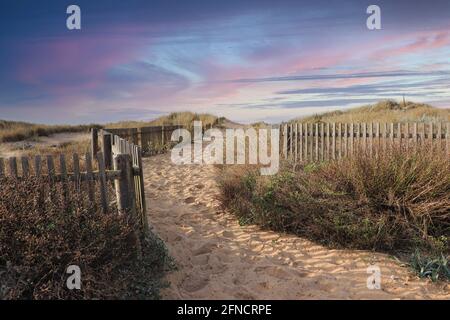 Path to the beach through the dunes surrounded by a wood fence at the sunset Stock Photo
