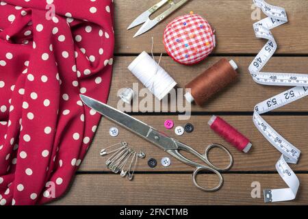 Sewing accessories and fabric on wooden background. Sewing threads, needles, pins, fabric, buttons and sewing centimeters. top view. Stock Photo