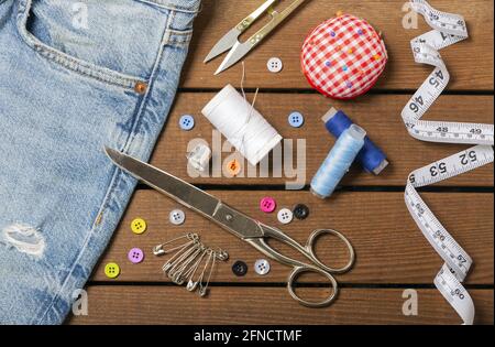Blue jeans and sewing tools kit on wooden textured background - concept Stock Photo