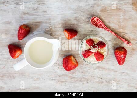 Glass of overnight oats with strawberries and milk jug on wooden background Stock Photo