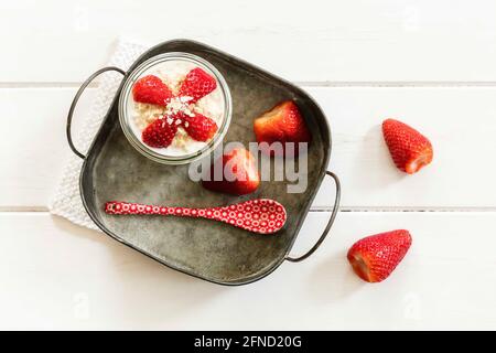 Glass of overnight oats with strawberries and milk jug on wooden background Stock Photo
