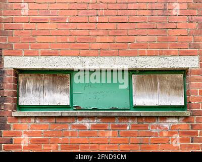 Three boarded up windows set in red brick wall Stock Photo