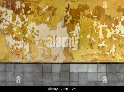 Peeling paint texture. Grunge wall background with cracked and peeled yellow paint and grey tiles Stock Photo