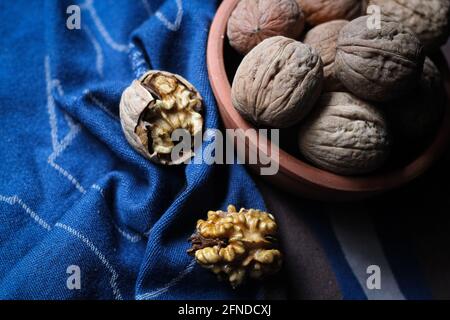Shelled and cracked walnuts scattered from the bowl on a blue and brown cotton kitchen cloth were photographed in dark mode. Creative concept composit Stock Photo