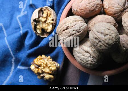 Shelled and cracked walnuts scattered from the bowl on a blue and brown cotton kitchen cloth were photographed in dark mode. Creative concept composit Stock Photo