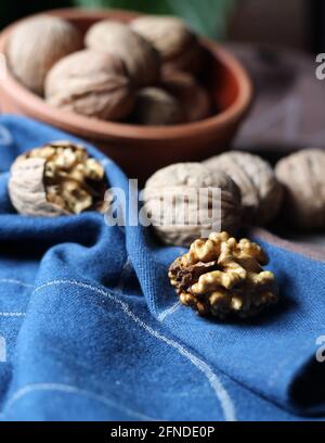 Shelled and cracked walnuts scattered from the bowl on a blue and brown cotton kitchen cloth were photographed in dark mode. Creative concept composit Stock Photo