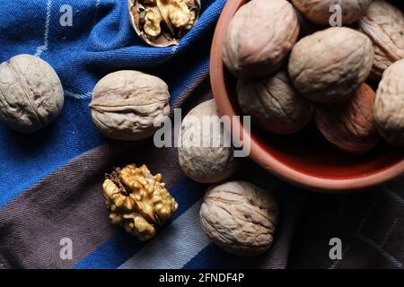 Shelled and cracked walnuts scattered from the bowl on a blue and brown cotton kitchen cloth were photographed in dark mode. Creative concept. Stock Photo