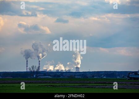 A view of the smoking chimneys of a distant coal-fired power plant on the horizon. Photo taken in natural daylight, late afternoon. Stock Photo