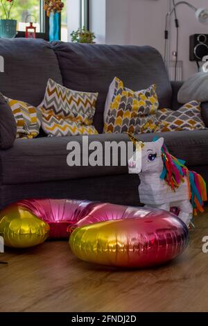 A White Unicorn Pinata And A colourful Number Three Balloon In A Living Room By A Sofa Stock Photo