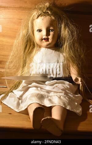 A vertical shot of a creepy old doll with a knife on the wooden chair Stock Photo