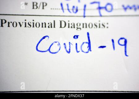a selective focus a handwritten report with a provisional diagnosis that is as covid-19 case, a handwritten text on a white paper with a provisional d Stock Photo