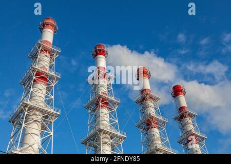 Four industrial chimneys against a blue sky. White smoke comes from several of them. Stock Photo