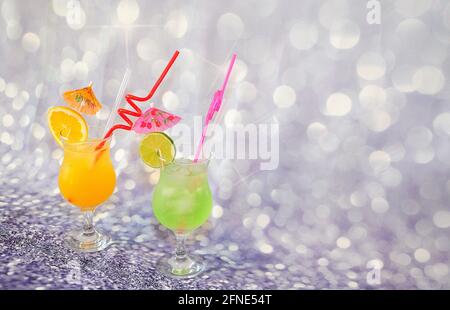 Two tall glasses with orange and lime juice, decorated with citrus slices with ice on a gray abstract background. Close-up. Stock Photo