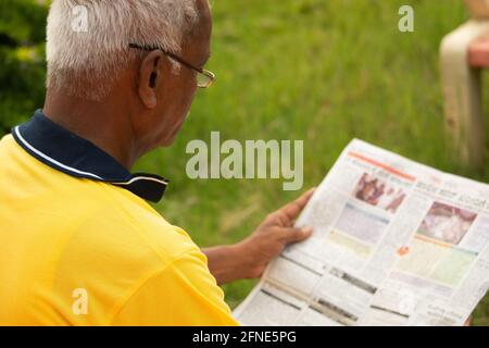 Focus on shoulder, Shoulder shot of old man busy reading morning news paper - Concept of senior people morning daily lifestyle. Stock Photo