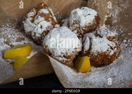 Four beignets are served on brown paper with lemon slices and covered in powdered sugar. Stock Photo