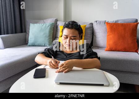 Asian woman writing note and work from home with laptop Stock Photo