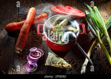 Maultaschen soup in the pot, Maultaschen in the broth, decorated with fresh vegetables Stock Photo