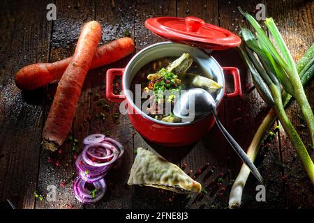 Maultaschen soup in the pot, Maultaschen in the broth, decorated with fresh vegetables Stock Photo