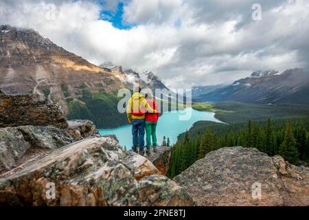 Couple hugging, looking into the distance, view of turquoise glacial lake surrounded by forest, Peyto Lake, Rocky Mountains, Banff National Park Stock Photo