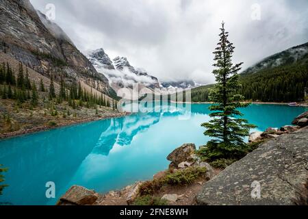 Clouds hanging between mountain peaks, reflection in turquoise glacial lake, Moraine Lake, Valley of the Ten Peaks, Rocky Mountains, Banff National Stock Photo