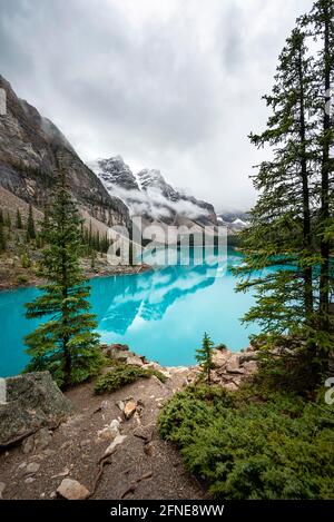 Clouds hanging between mountain peaks, reflection in turquoise glacial lake, Moraine Lake, Valley of the Ten Peaks, Rocky Mountains, Banff National Stock Photo