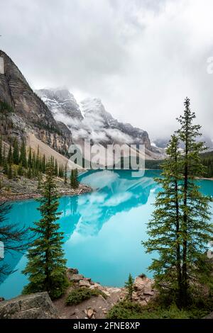 Clouds hanging between mountain peaks, reflection in turquoise glacial lake, Moraine Lake, Valley of the Ten Peaks, Rocky Mountains, Banff National Stock Photo