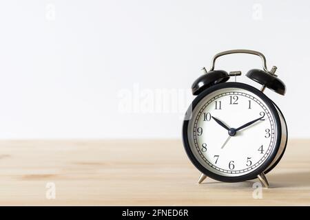 Classic vintage black alarm clock on wooden table with white wall background and copy space for text. Time concept. Stock Photo