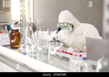 Scientist in PPE mask and goggles doing research and working with microscope in laboratory Stock Photo