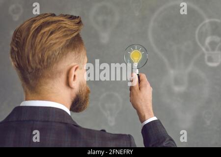Man with magnifying glass looking at yellow light bulb as symbol of business idea Stock Photo