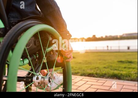 A disabled man is sitting in a wheelchair. He holds his hands on the wheel. Stock Photo