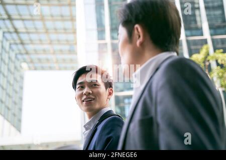 two asian business people walking talking on street in modern city Stock Photo